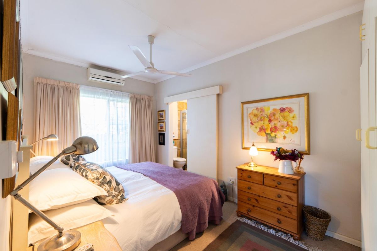 A well-maintained bedroom featuring a ceiling fan, split-system air conditioning, and an en-suite bathroom accessed via a sliding door.