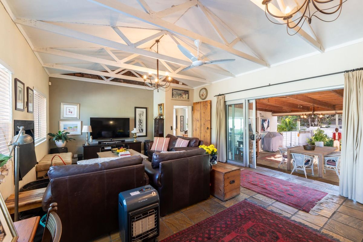 Spacious living room featuring exposed timber roof trusses, stone tile flooring, and large sliding glass doors that open onto a covered patio area.