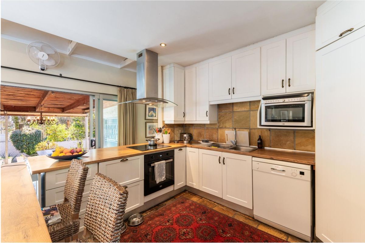 A functional kitchen featuring white cabinetry, wooden countertops, built-in appliances, and a stone tile backsplash, with direct access to an outdoor patio area.