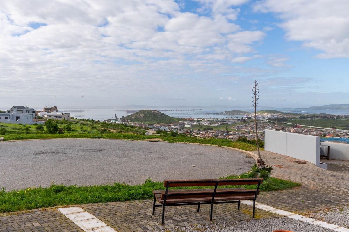 Elevated view overlooking the surrounding residential area, coastline, and bay, featuring a paved driveway and retaining wall on the property.