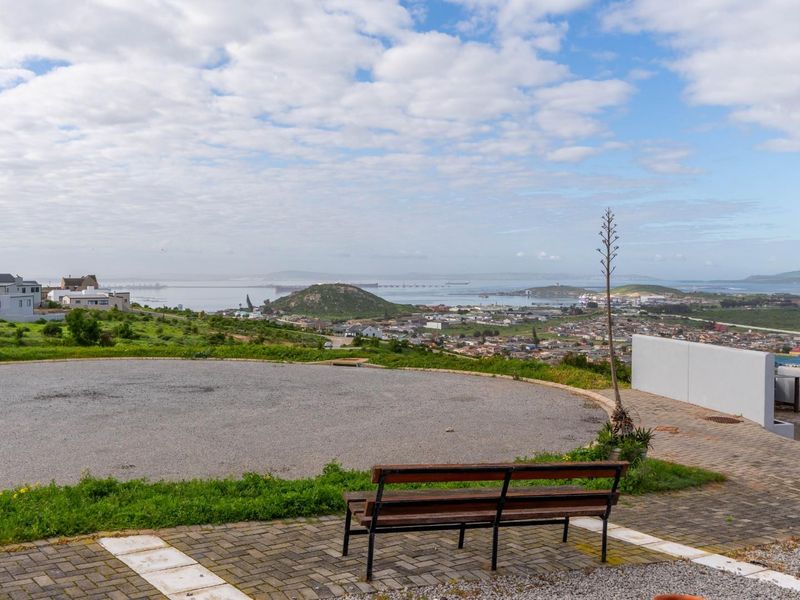 Elevated view overlooking the surrounding residential area, coastline, and bay, featuring a paved driveway and retaining wall on the property.