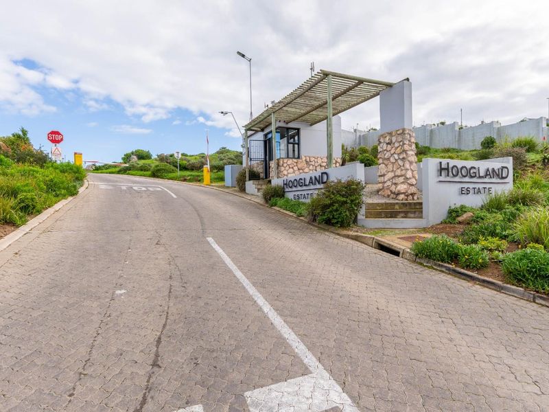 The entrance to Hoogland Estate featuring a paved driveway, security gatehouse with stone cladding, and established landscaping.