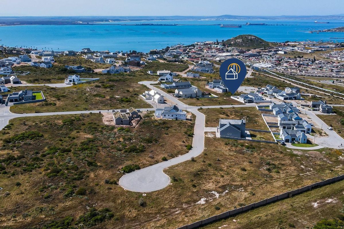 Aerial view of a residential development site featuring paved roads and coastal views, showcasing the surrounding neighborhood and landscape.