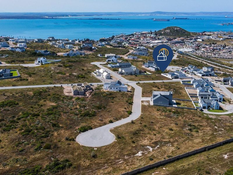 Aerial view of a residential development site featuring paved roads and coastal views, showcasing the surrounding neighborhood and landscape.