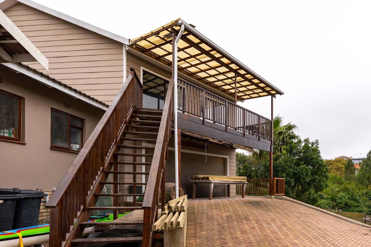 Rear exterior view featuring a raised timber deck with a polycarbonate roof, external timber staircase, and paved driveway area.