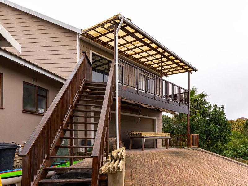 Rear exterior view featuring a raised timber deck with a polycarbonate roof, external timber staircase, and paved driveway area.