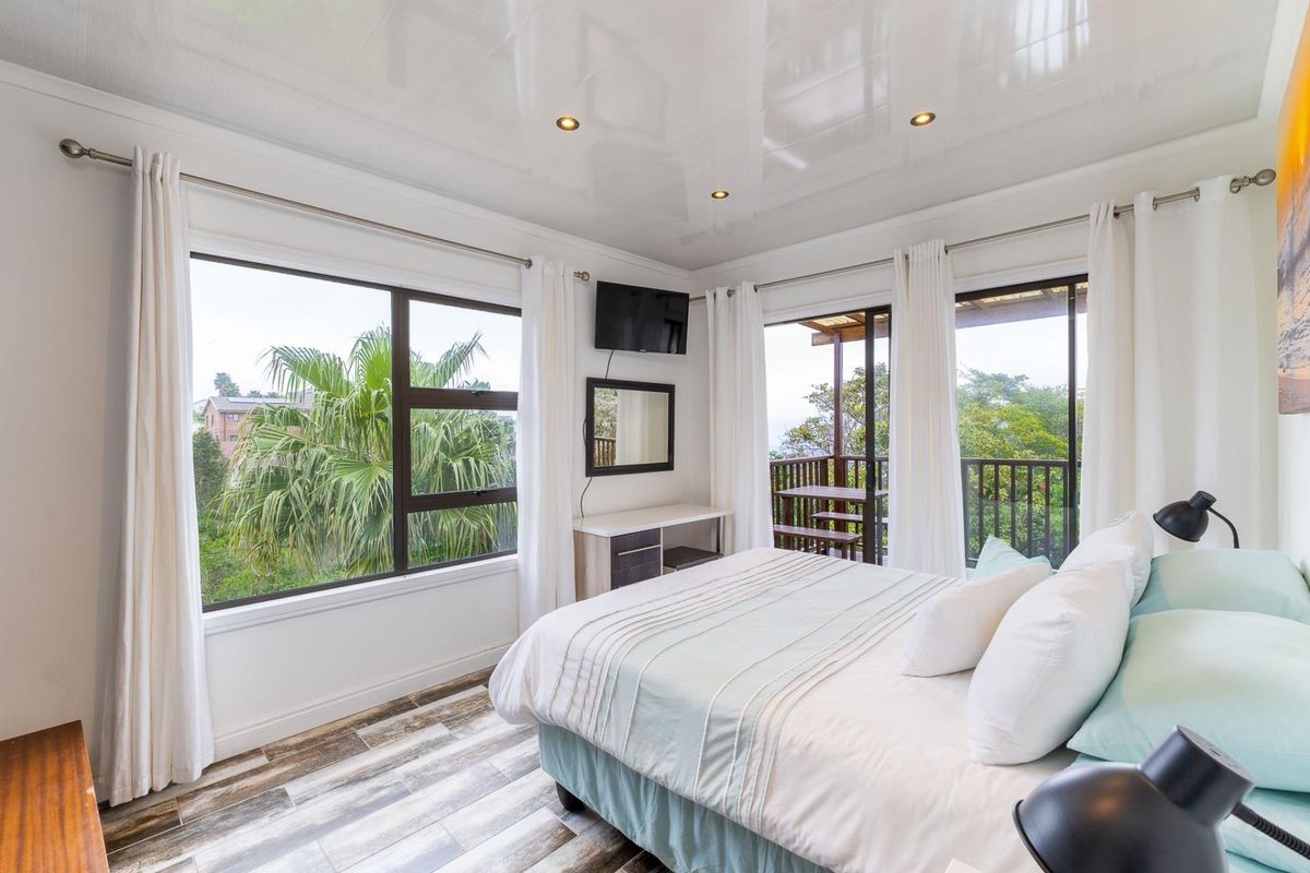 Bright bedroom featuring wood-look tile flooring, recessed downlights, and direct access to a private balcony through sliding glass doors.