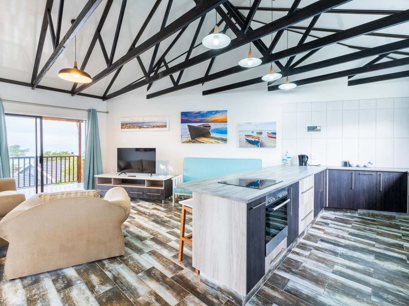 Spacious open-plan living area featuring exposed timber roof trusses, a modern kitchen with island, and direct access to a private balcony.