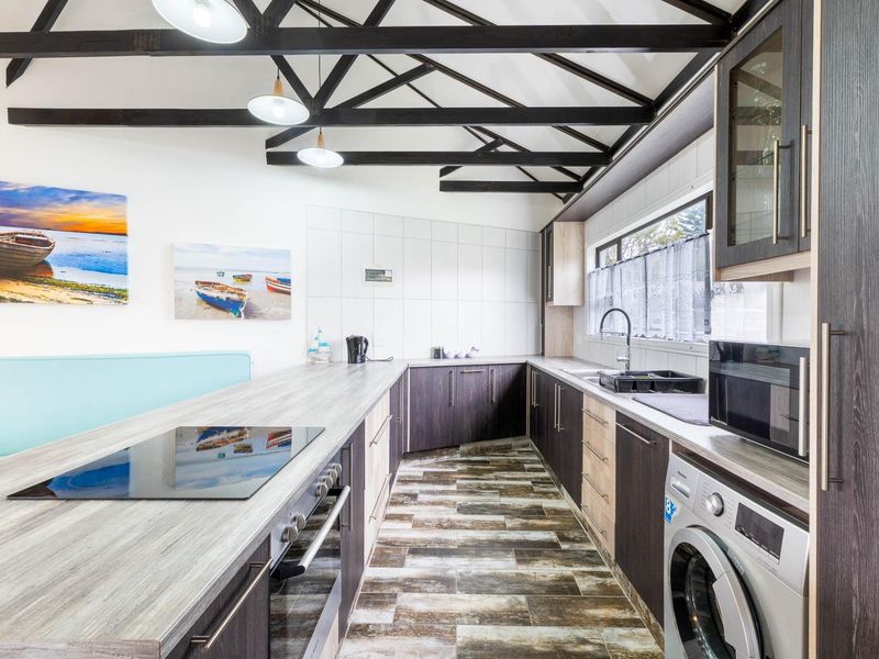 Modern kitchen featuring exposed timber ceiling beams, sleek dark cabinetry, integrated appliances, and a functional layout with ample counter space.