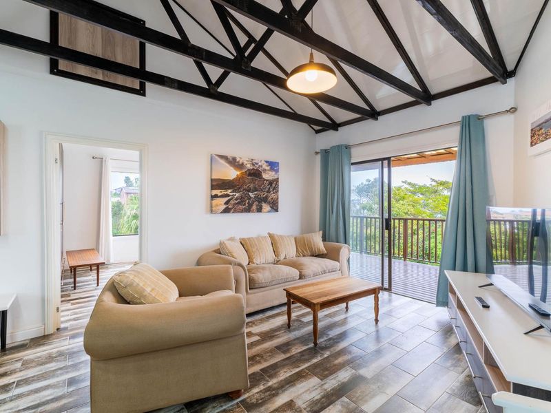 Bright living room featuring exposed timber roof trusses, tiled flooring, and direct access to a balcony through sliding glass doors.