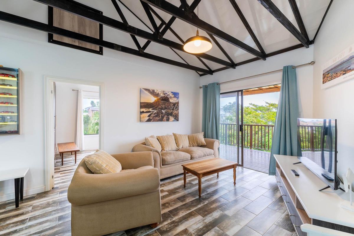 Bright living room featuring exposed timber roof trusses, tiled flooring, and direct access to a balcony through sliding glass doors.