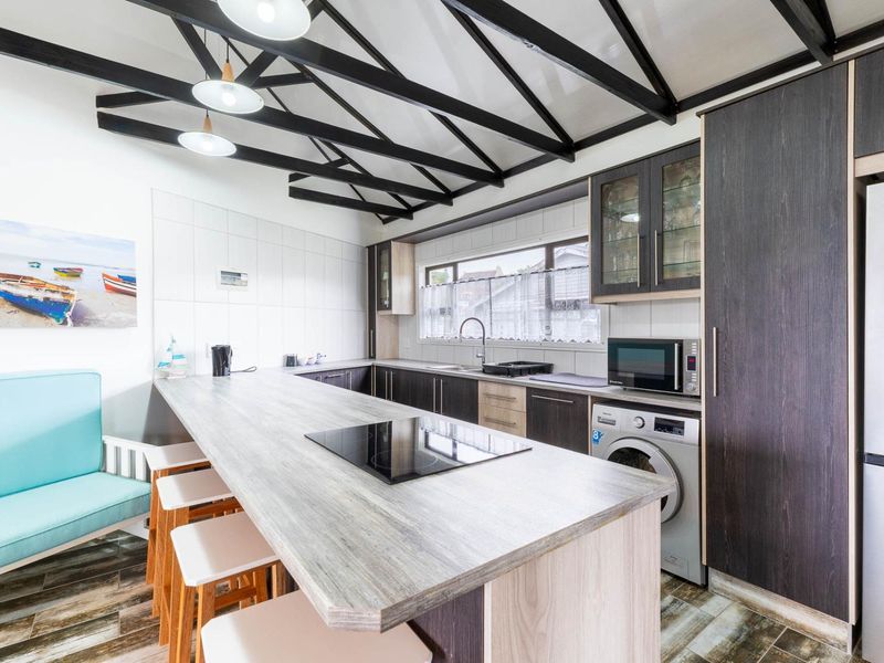 Modern kitchen featuring dark wood cabinetry, a large island with an integrated induction cooktop, exposed ceiling beams, and built-in laundry appliances.