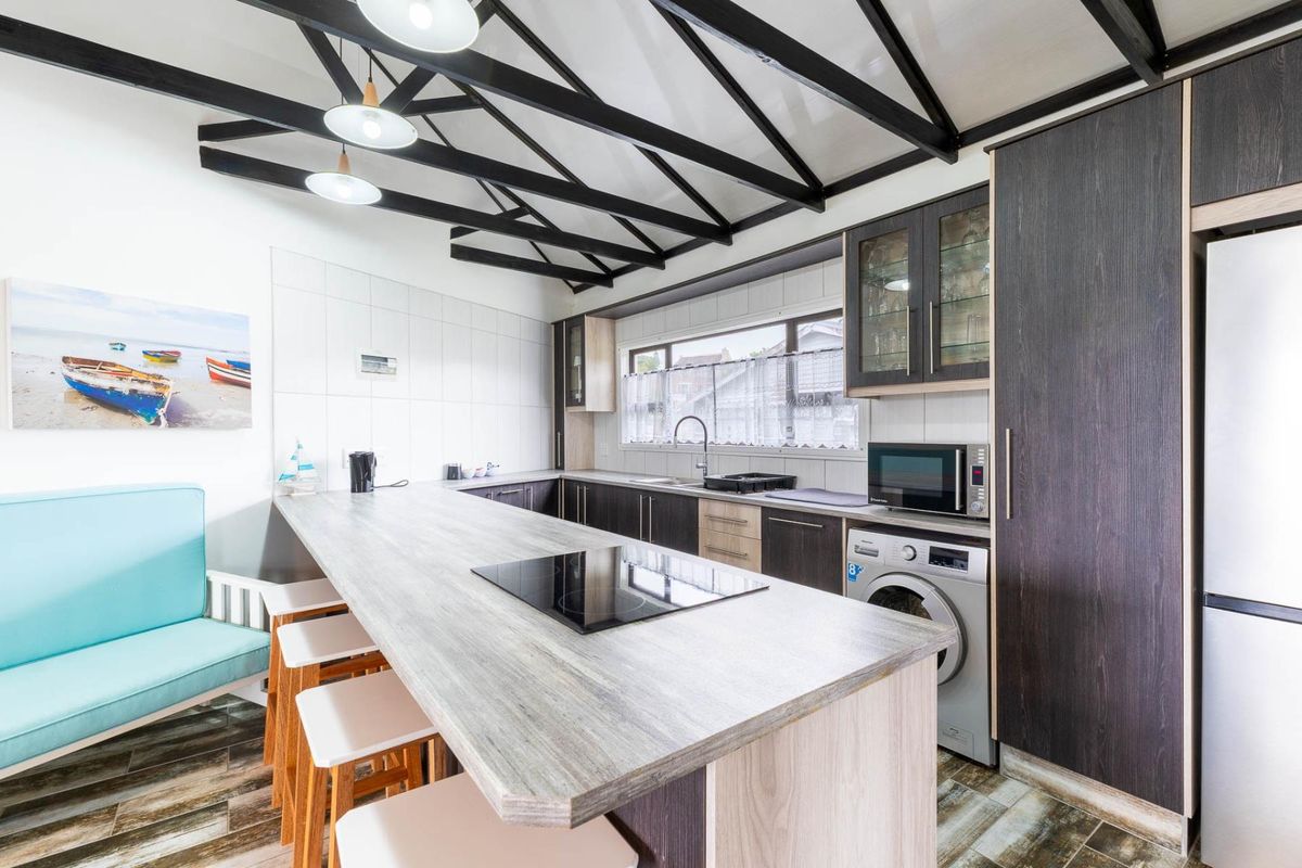 Modern kitchen featuring dark wood cabinetry, a large island with an integrated induction cooktop, exposed ceiling beams, and built-in laundry appliances.