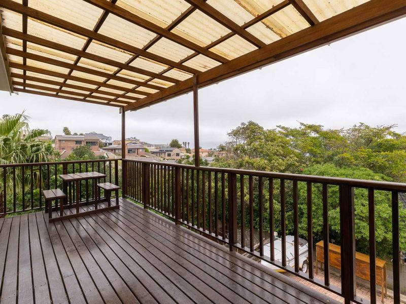 Covered timber balcony featuring a pergola roof structure and balustrade, offering an elevated outdoor space with neighbourhood views.
