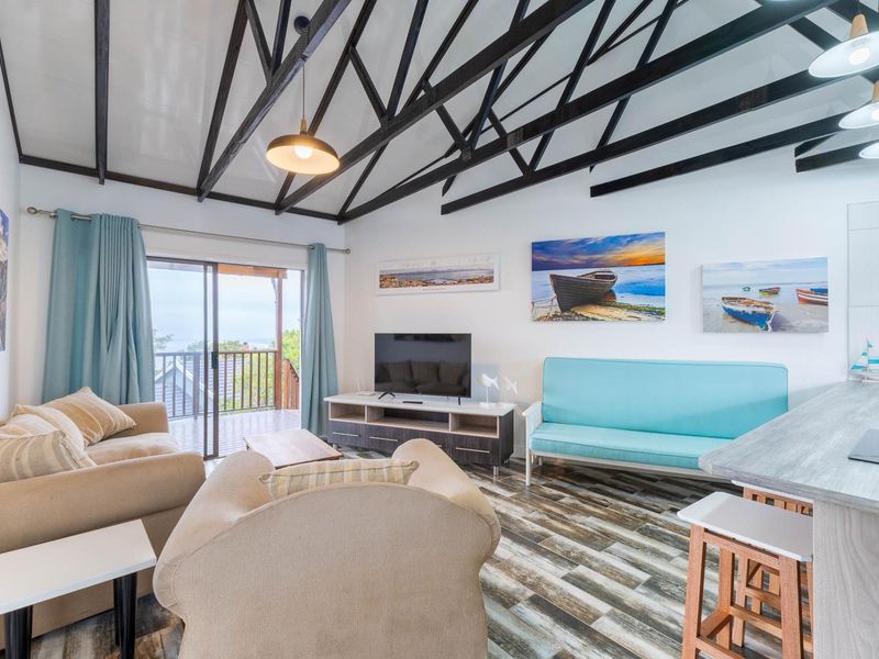 Open-plan living area featuring a vaulted ceiling with exposed timber trusses, wood-look tile flooring, and direct access to a balcony through sliding glass doors.