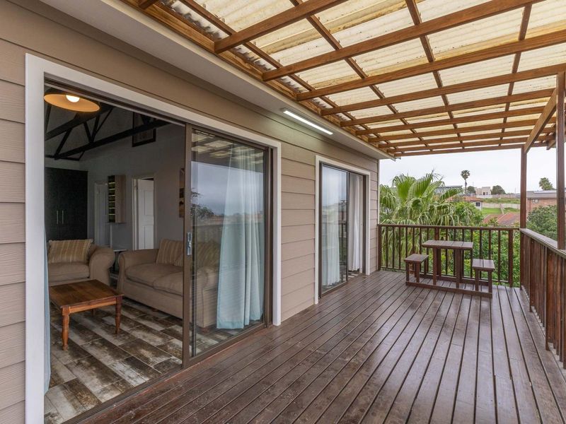 A spacious covered balcony featuring timber decking, a pergola-style roof, and sliding glass doors providing seamless access to the interior living area.