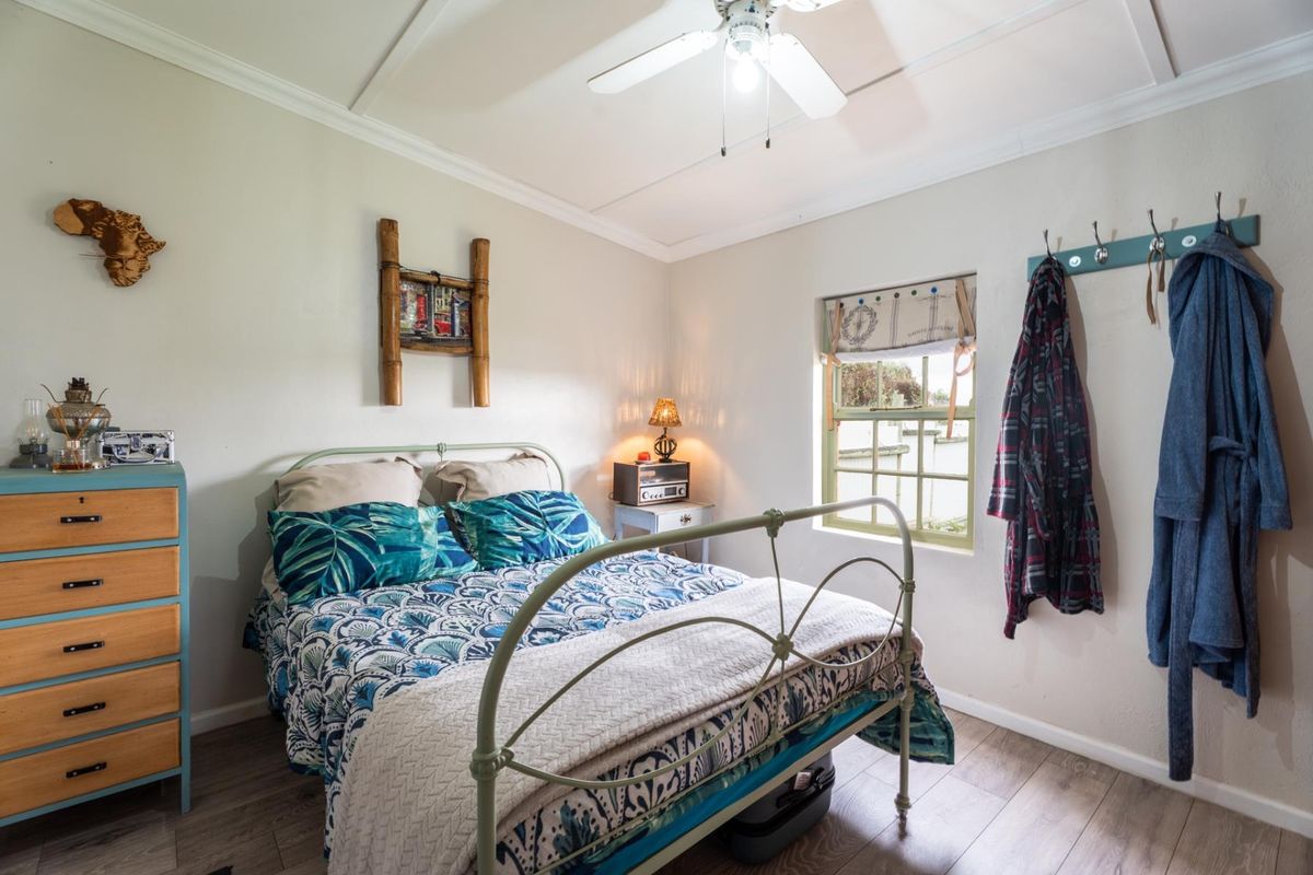 A cozy bedroom featuring laminate flooring, a ceiling fan, and a multi-pane window, offering a comfortable and functional living space.