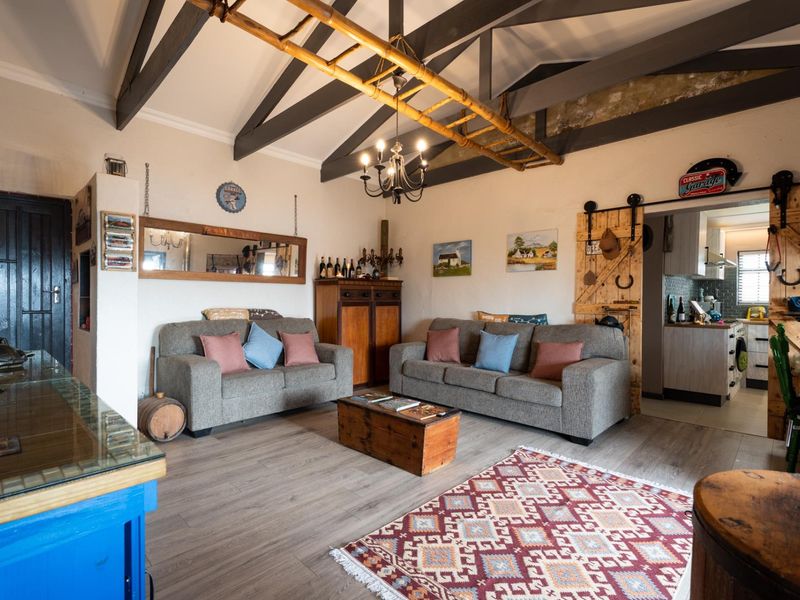 Spacious open-plan living area featuring high vaulted ceilings with exposed timber trusses, laminate flooring, and a rustic sliding barn door leading to the kitchen.