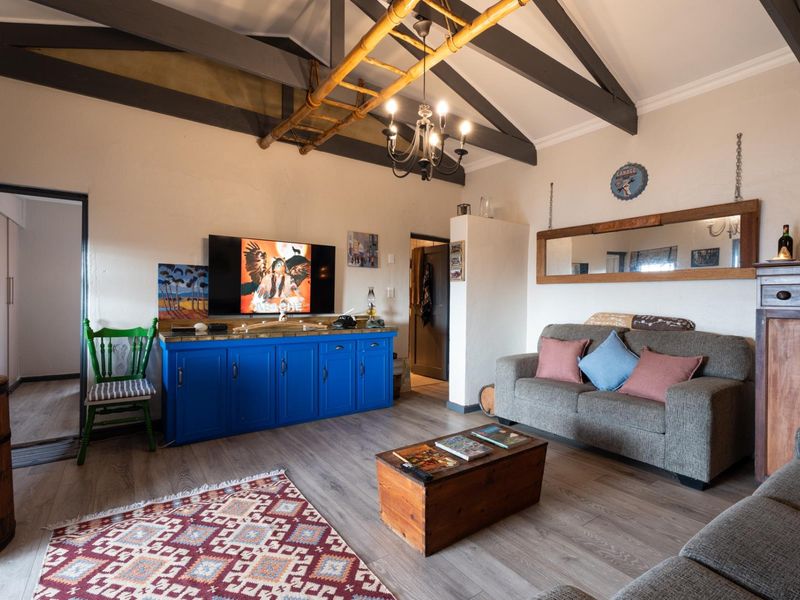 A cozy living room featuring vaulted ceilings with exposed timber beams, laminate flooring, and a classic chandelier, creating a warm and inviting atmosphere.