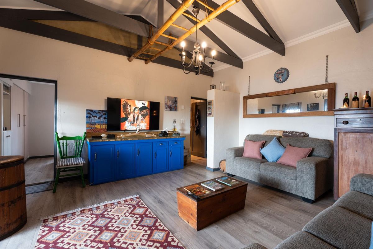 A cozy living room featuring vaulted ceilings with exposed timber beams, laminate flooring, and a classic chandelier, creating a warm and inviting atmosphere.