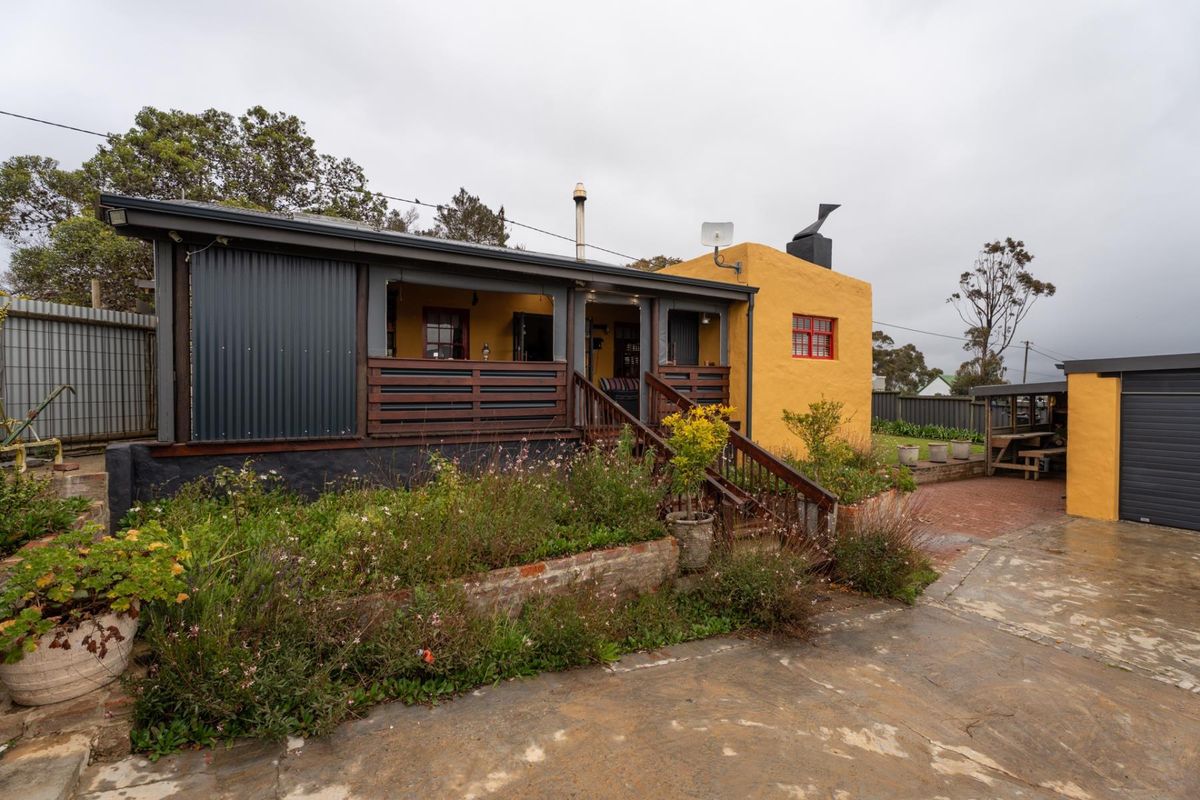Rear view of the property featuring a timber deck, corrugated metal siding, yellow rendered walls, and a paved courtyard area.