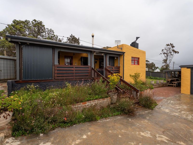 Rear view of the property featuring a timber deck, corrugated metal siding, yellow rendered walls, and a paved courtyard area.