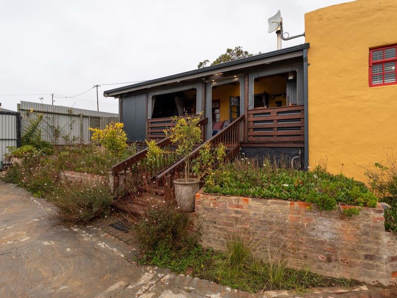 Rear exterior view featuring a raised timber deck with staircase, brick retaining wall, and corrugated metal siding on the building facade.