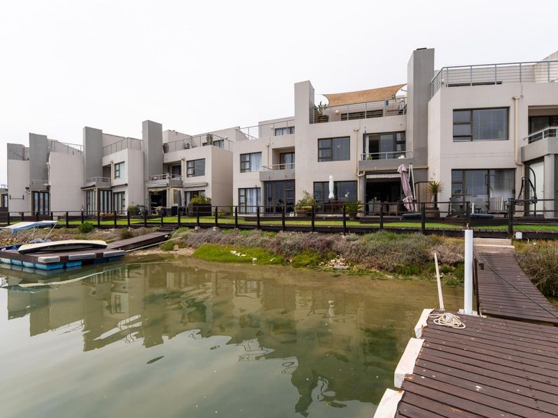 Rear view of the townhouse complex featuring private timber jetties, direct water access, and multi-level balconies with sliding door access.