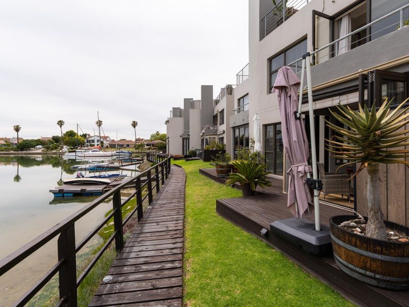 Rear view of the townhouse featuring a private timber deck, lawn area, and direct access to the waterfront boardwalk and jetty.