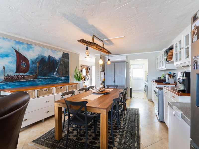 An open-plan dining and kitchen area featuring tiled flooring, built-in cabinetry with timber countertops, and a rustic timber pendant light fixture.