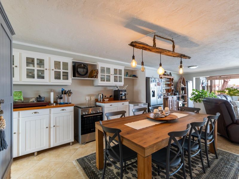 Open-plan kitchen and dining area featuring white cabinetry, timber countertops, tiled flooring, and a rustic pendant light fixture.