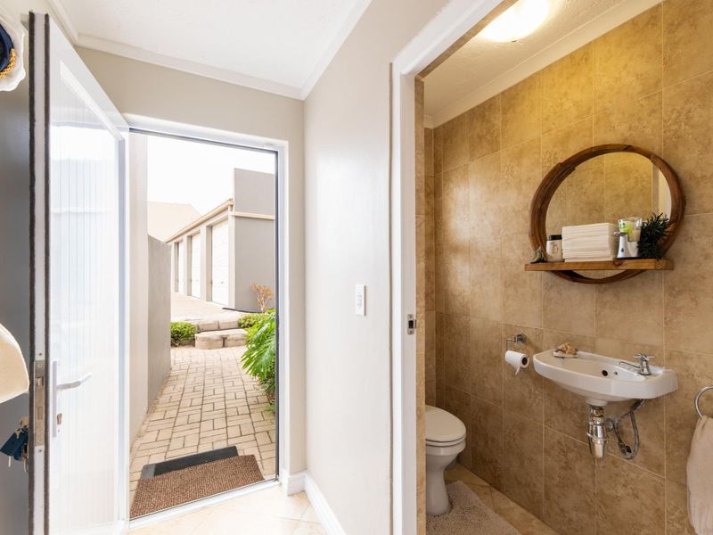 A compact guest bathroom featuring tiled walls, a wall-mounted basin, and a toilet, with direct access to an outdoor paved walkway.