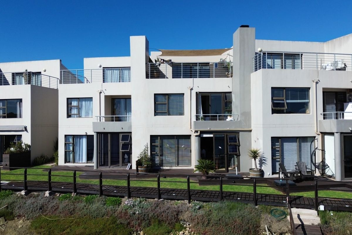 Rear elevation of a multi-level townhouse complex featuring timber decking, private balconies, and direct access to a landscaped boardwalk area.