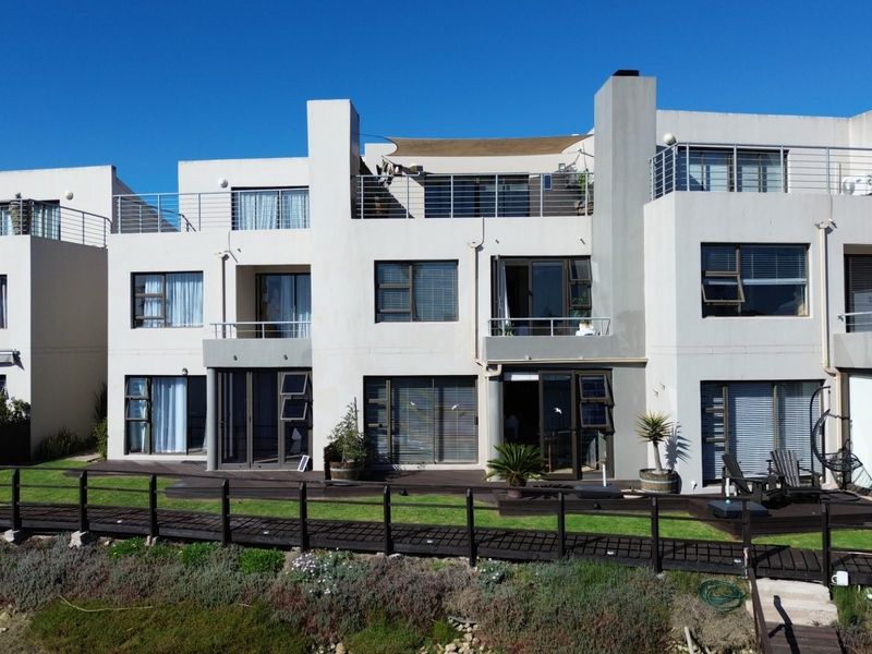 Rear elevation of a multi-level townhouse complex featuring timber decking, private balconies, and direct access to a landscaped boardwalk area.