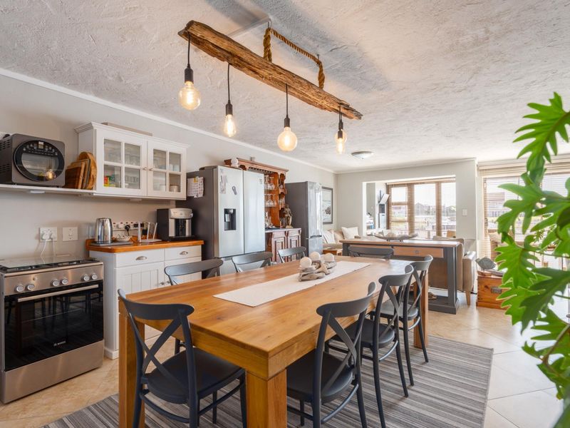 Open-plan kitchen and dining area featuring tiled flooring, built-in cabinetry, and a distinctive timber beam light fixture over the dining space.