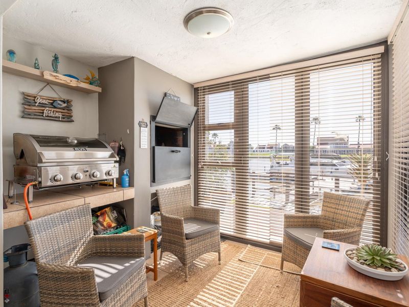 Enclosed patio area featuring a built-in braai, tiled prep surface, and large windows with venetian blinds offering a view of the marina.
