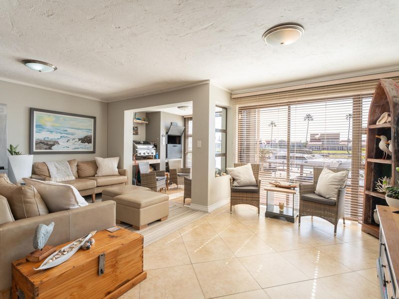 Spacious open-plan living area featuring tiled floors, large windows with natural light, and a built-in braai area, perfect for relaxed coastal living.