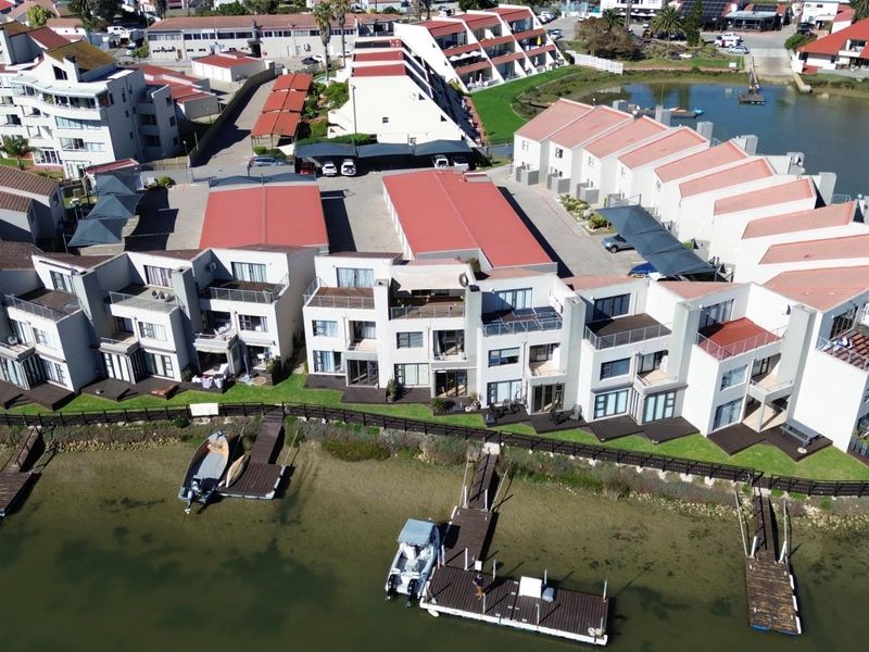 Aerial view of a waterfront townhouse complex featuring private jetties, landscaped grounds, and dedicated parking areas within a secure estate.