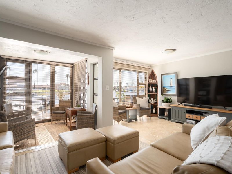 A bright and spacious living area featuring tiled flooring, large windows with venetian blinds, and a comfortable layout overlooking the exterior.