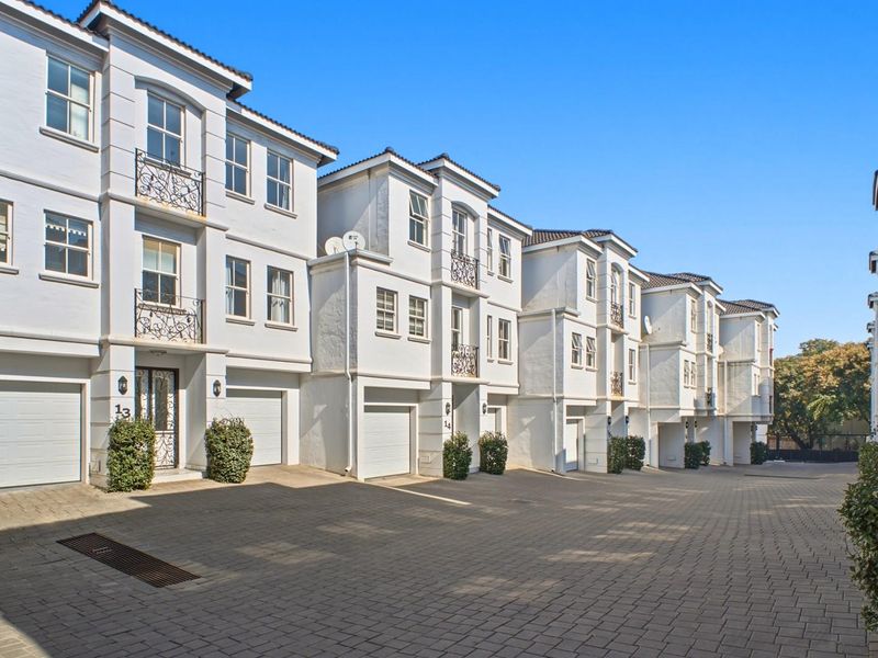 A row of multi-story townhouses featuring white facades, paved driveway access, and integrated garages within a well-maintained residential complex.