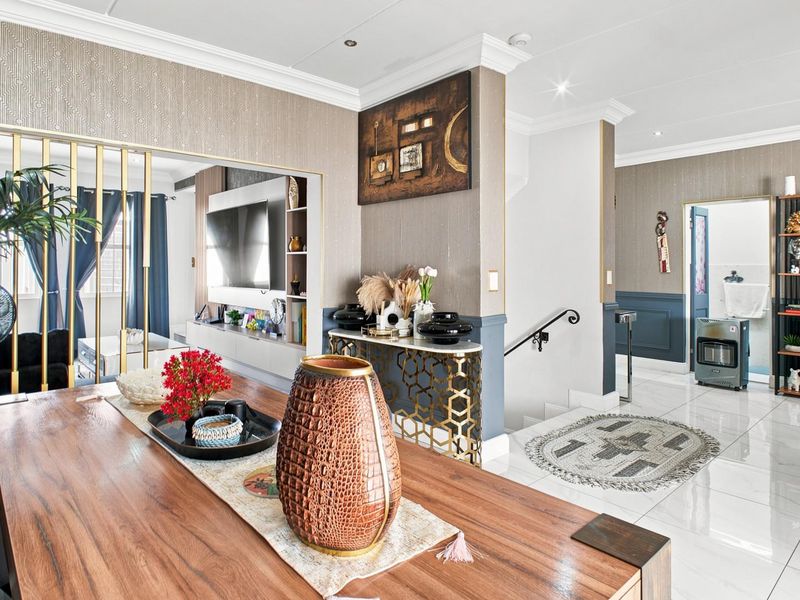 A well-maintained open-plan living and dining area featuring polished tiled floors, decorative wall paneling, and a staircase with a modern metal handrail.