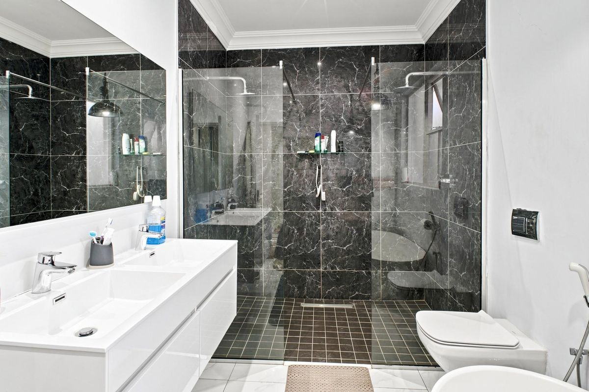 Modern bathroom featuring a double vanity, large wall mirror, and a spacious walk-in shower with dark marble-look tiling.