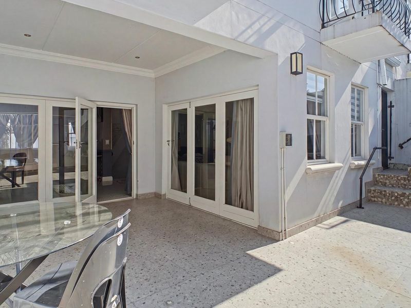 A spacious covered patio featuring terrazzo flooring, multiple sets of french doors providing indoor-outdoor flow, and stone-clad steps leading to an upper level.