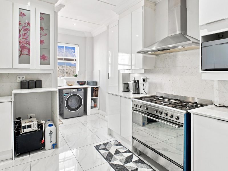 Modern kitchen featuring white gloss cabinetry, marble-look countertops, a gas stove with extractor fan, and integrated laundry space with tiled flooring.
