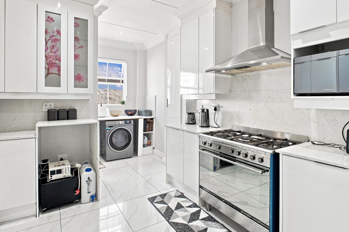 Modern kitchen featuring white gloss cabinetry, marble-look countertops, a gas stove with extractor fan, and integrated laundry space with tiled flooring.