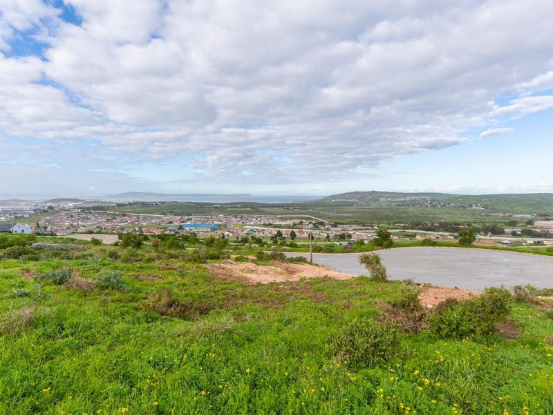 Elevated view overlooking a residential area and coastal landscape from a vacant plot with an existing paved cul-de-sac.