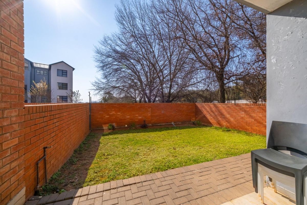 A private rear garden featuring a paved patio area and a small lawn enclosed by brick boundary walls.