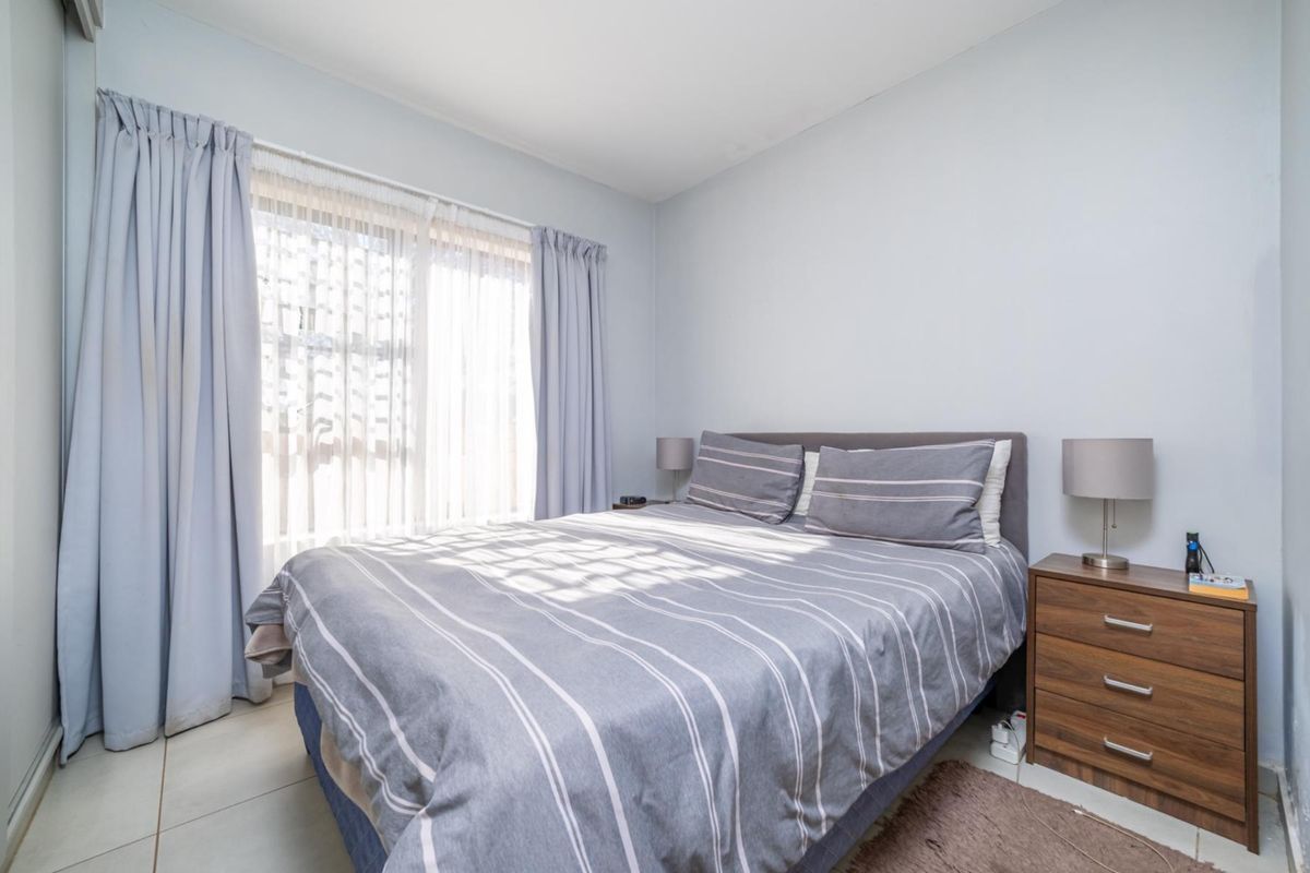 A functional bedroom featuring tiled flooring and large windows with curtain tracks, providing natural light.