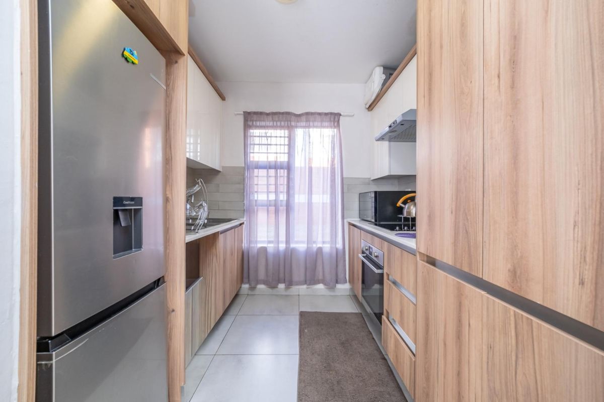 A modern galley-style kitchen featuring wood-grain cabinetry, built-in oven, extractor fan, and tiled flooring with a clean, functional layout.
