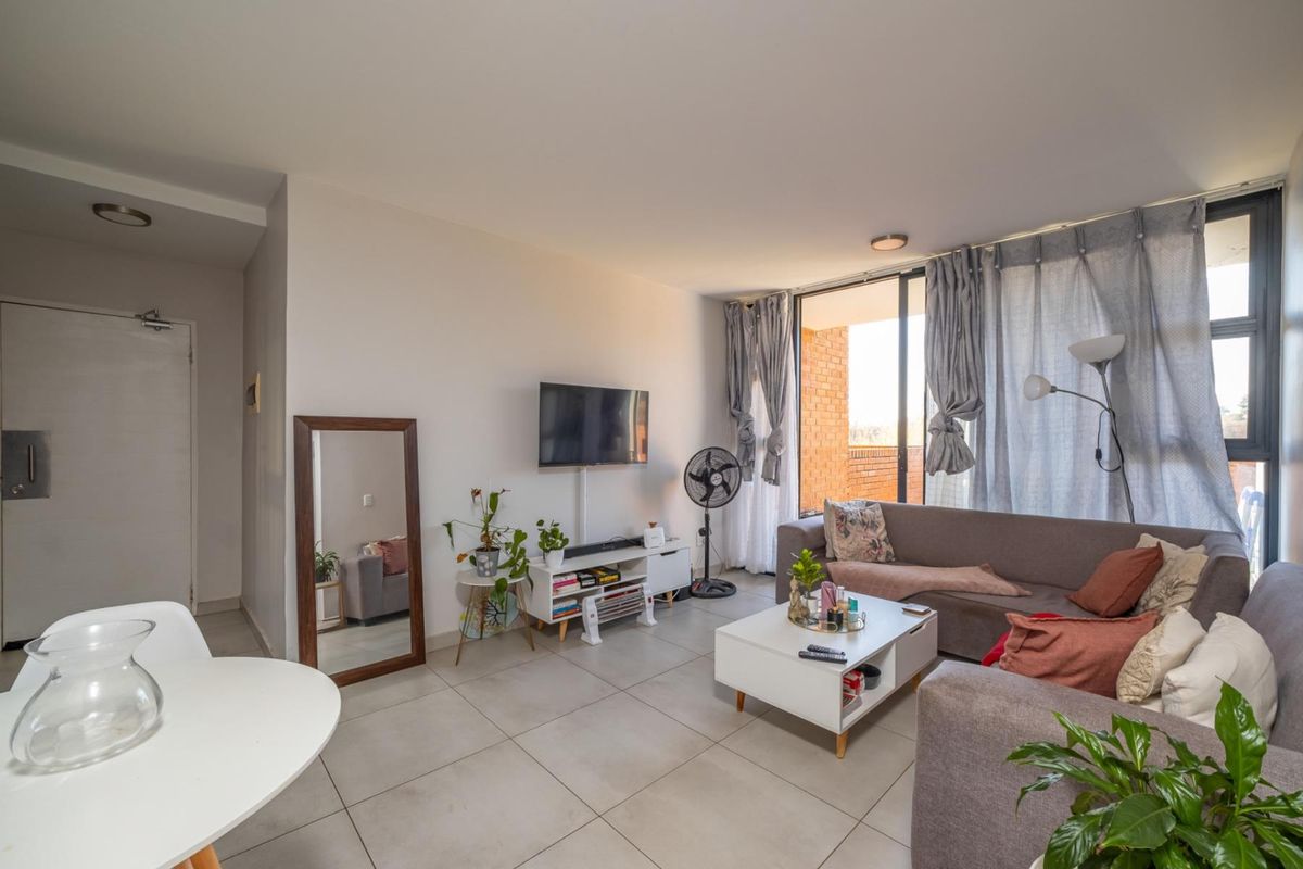 A bright, open-plan living area featuring neutral tiled flooring and a large sliding glass door providing access to an outdoor balcony.